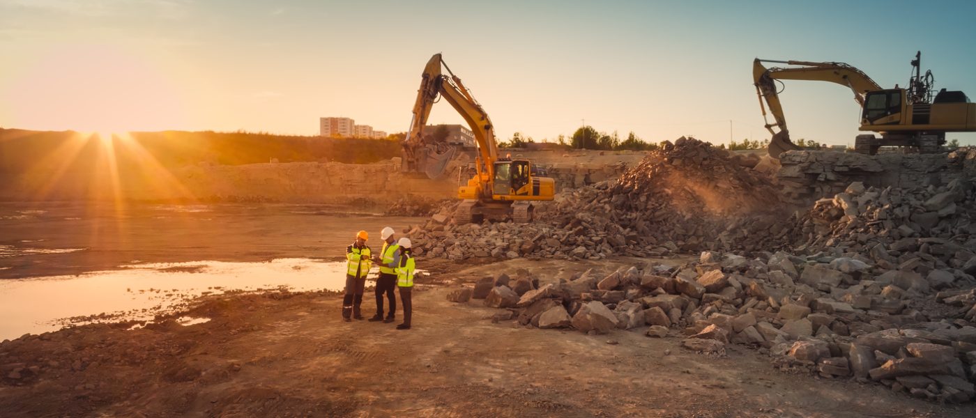 Aerial Drone Shot Of Construction Site With Excavators On Sunny Day: Diverse Team of Real Estate Developers Discussing Project. Civil Engineer, Architect, Inspector Talking And Using Tablet Computer.